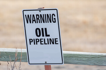 A generic Warning Oil Pipeline sign at a wooden farm fence