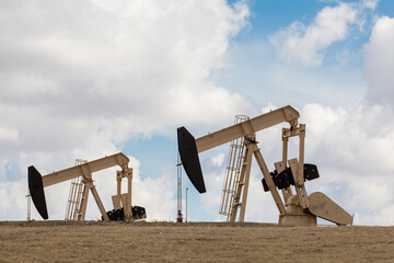 Two oil field pumpjacks, or donkeys, in an oil field against a cloudy sky