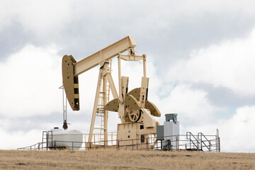 Fototapeta na wymiar A beige color oil field pumpjack, or donkey, in an oil field against a cloudy sky 