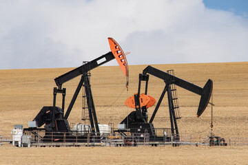 Two colorful black and orange oil field pumpjacks, or donkeys, in a dirt field against a cloudy sky