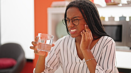 African american woman drinking water sitting on table suffering for toothache at dinning room