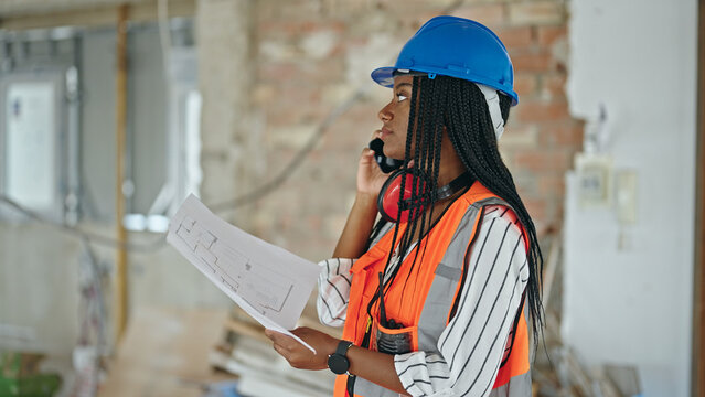 African american woman builder reading house project talking by smartphone at construction site