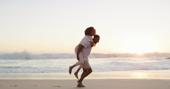 Black couple, piggyback and walking on beach in sunset for bonding, love or enjoying holiday together outdoors. Happy African man carrying woman on back for walk in joyful happiness on a ocean coast