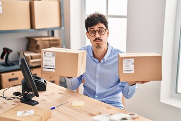 Hispanic man working at small business ecommerce holding packages puffing cheeks with funny face....