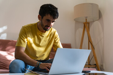 Young man using a laptop computer while sitting on a sofa at home