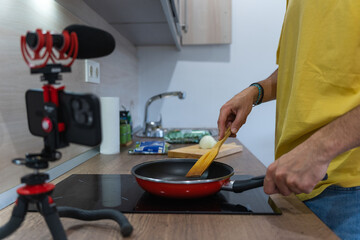 Unrecognizable man cooking in a modern kitchen at home while recording himself with a smart phone and microphone. Man preparing food on the pan and recording it for a vblog or social media.