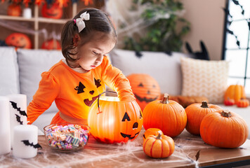 Adorable hispanic girl wearing pumpkin costume holding candies of pumpkin basket at home