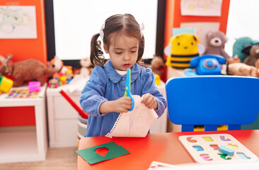 Adorable hispanic girl student cutting paper at kindergarten