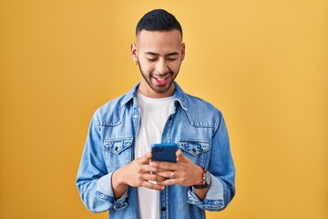 Young hispanic man using smartphone typing message winking looking at the camera with sexy...