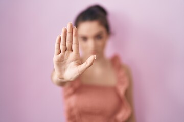 Obraz na płótnie Canvas Young teenager girl standing over pink background doing stop sing with palm of the hand. warning expression with negative and serious gesture on the face.