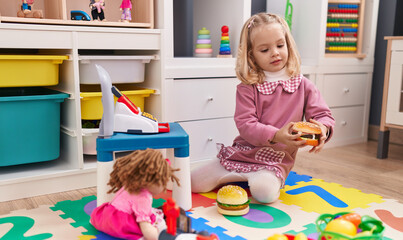 Adorable blonde girl playing supermarket toys sitting on floor at kindergarten