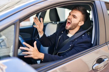 Young hispanic man stressed driving car at street