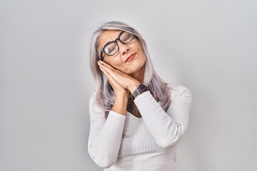 Middle age woman with grey hair standing over white background sleeping tired dreaming and posing...