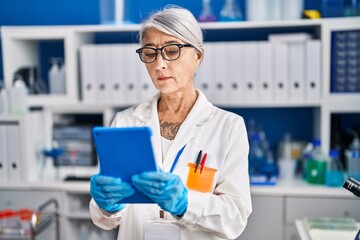 Middle age grey-haired woman scientist using touchpad working at laboratory