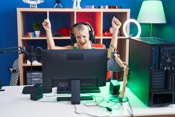 Young blonde woman streamer playing video game with winner expression at gaming room