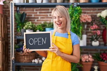 Young caucasian woman working at florist holding open sign winking looking at the camera with sexy...