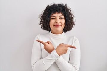 Hispanic woman with curly hair standing over isolated background pointing to both sides with fingers, different direction disagree - obrazy, fototapety, plakaty