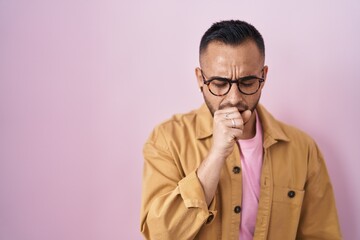 Young hispanic man standing over pink background feeling unwell and coughing as symptom for cold or bronchitis. health care concept.