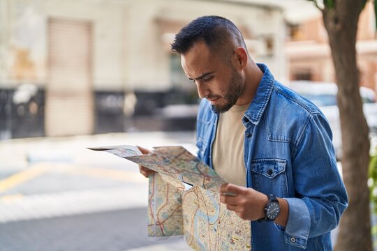 Young hispanic man looking city map at street