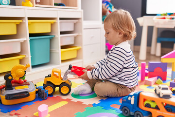 Adorable caucasian boy playing with tractor toy sitting on floor at kindergarten
