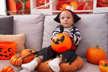 Adorable caucasian boy wearing pirate costume holding sweet on pumpkin basket at home