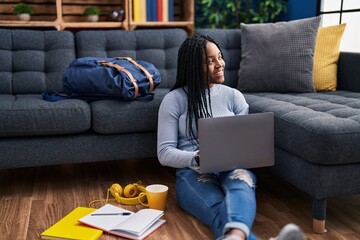 African american woman student sitting on floor using laptop at street