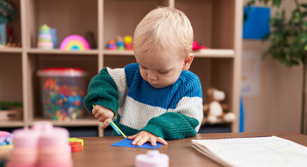 Adorable caucasian boy student cutting paper at kindergarten