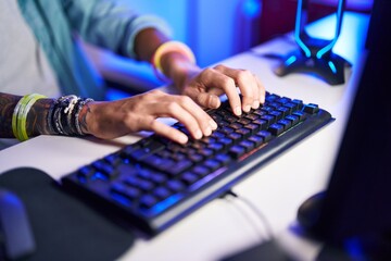 Young hispanic man using computer keyboard at gaming room