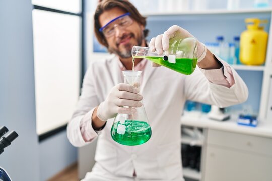 Middle age man scientist pouring liquid on test tube at laboratory