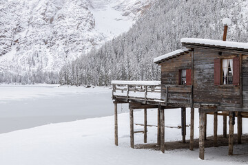Wooden hut by the frozen Braies Lake on a snowy winter day, Dolomites, Italy
