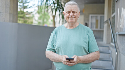 Middle age grey-haired man using smartphone smiling at street
