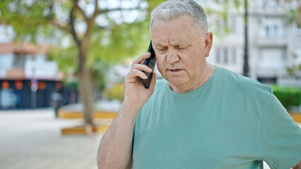 Middle age grey-haired man talking on smartphone with serious expression at park