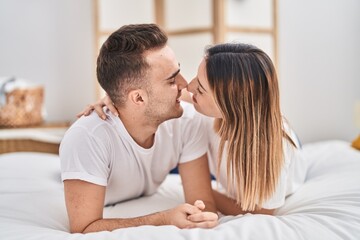 Man and woman couple lying on bed hugging each other and kissing at bedroom