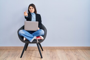 Young hispanic woman sitting on chair using computer laptop showing middle finger, impolite and...