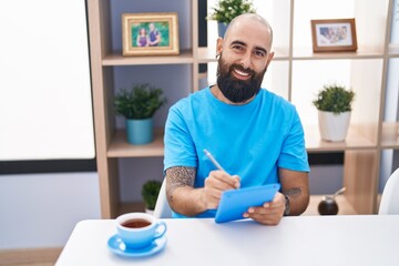 Young bald man using touchpad drinking coffee at home