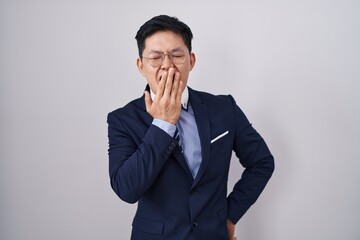 Young asian man wearing business suit and tie bored yawning tired covering mouth with hand....