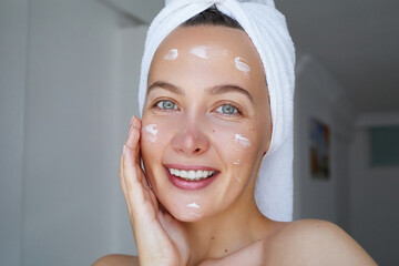 Young beautiful woman is applying  a cream, scrub beauty product on her face. Morning skin care...
