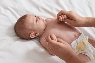 Adorable caucasian baby lying on bed holding mother hands at bedroom