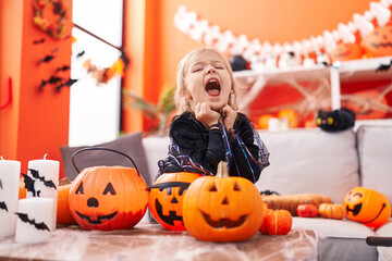 Adorable blonde girl wearing witch costume screaming at home