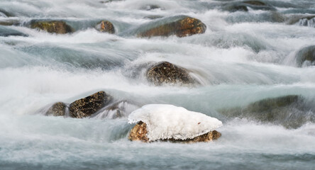 Winter river flowing over snow and ice covered stones, closeup detail, long exposure photo