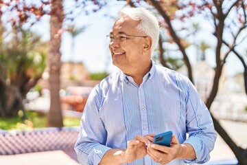 Senior man smiling confident using smartphone at park