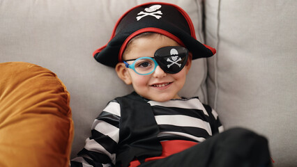 Adorable hispanic boy wearing pirate costume sitting on sofa at home