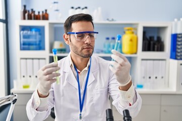 Young hispanic man scientist holding test tubes at laboratory
