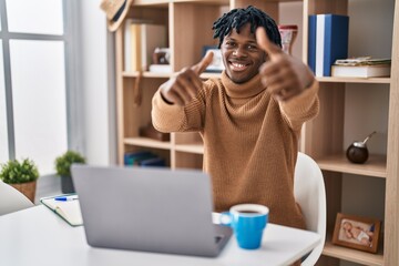 Young african man with dreadlocks working using computer laptop approving doing positive gesture with hand, thumbs up smiling and happy for success. winner gesture.