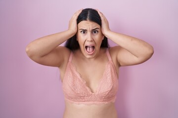Young hispanic woman wearing pink bra crazy and scared with hands on head, afraid and surprised of...