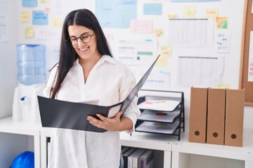 Young beautiful hispanic woman business worker reading document at office