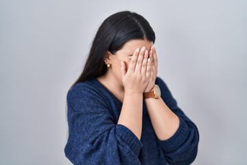 Young brunette woman standing over isolated background with sad expression covering face with hands...
