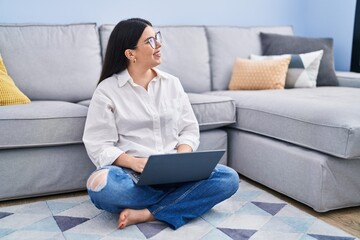 Young hispanic woman using laptop sitting on floor at home