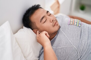 Young chinese man listening to music sleeping on bed at bedroom