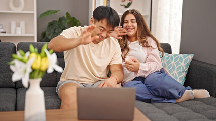 Man and woman couple sitting on sofa having video call drinking coffee at home